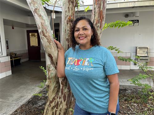 Ms. Diaz in the first grade courtyard wearing a green T shirt that reads Teacher Teach, Love, and Inspire