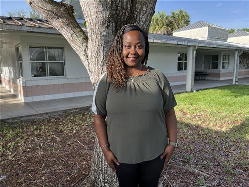 Mrs. Dyer standing outside the fourth grade building near a tree