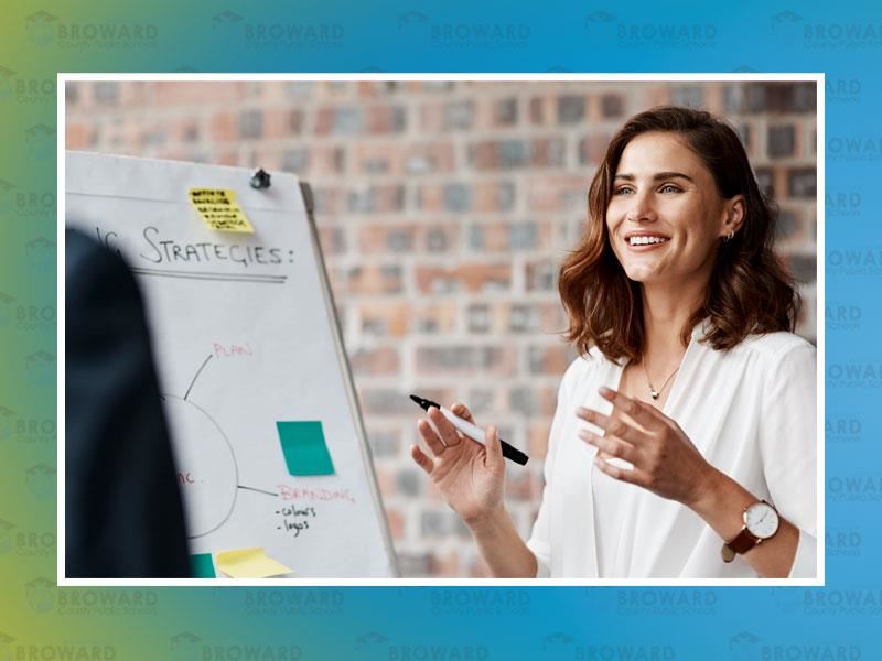 Woman standing in front of a board smiling  while doing a presentation